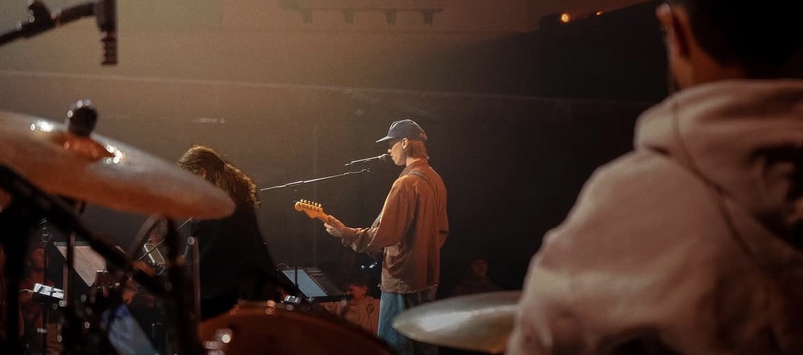 Owen performing on stage with a band under warm stage lighting