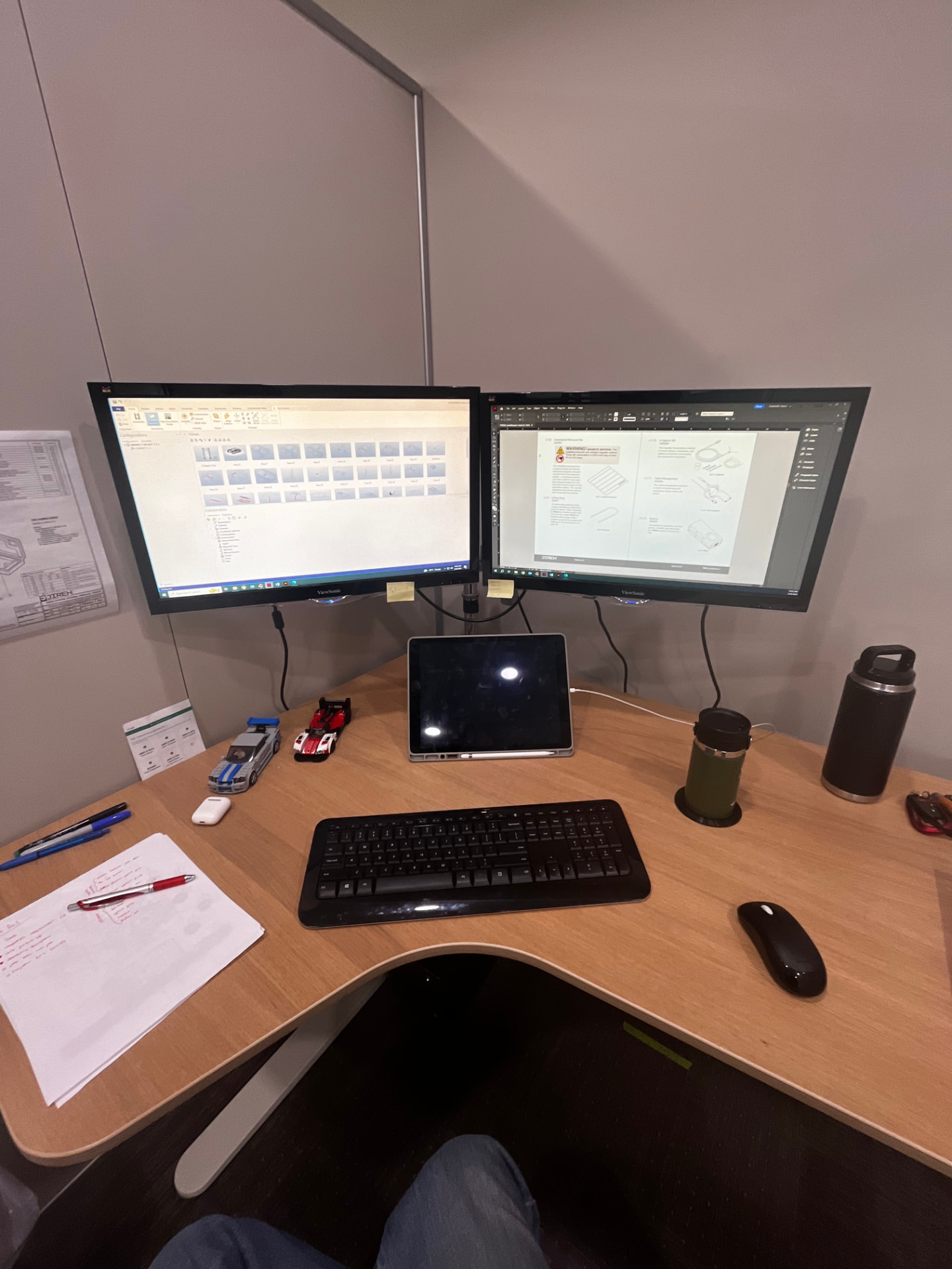 A dual-monitor desk setup with technical drawings and notes