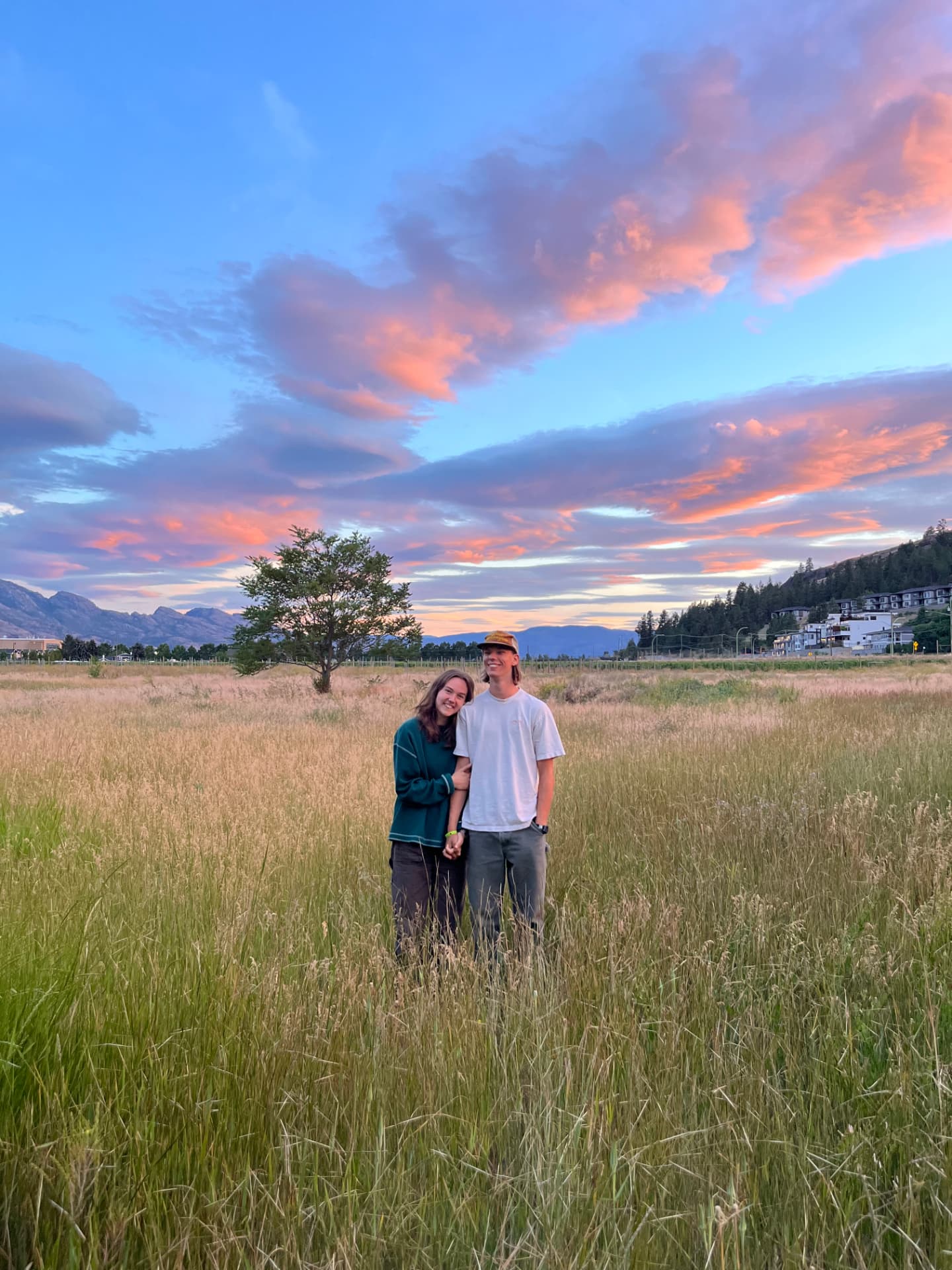 Owen and his partner standing in a tall grass field at sunset