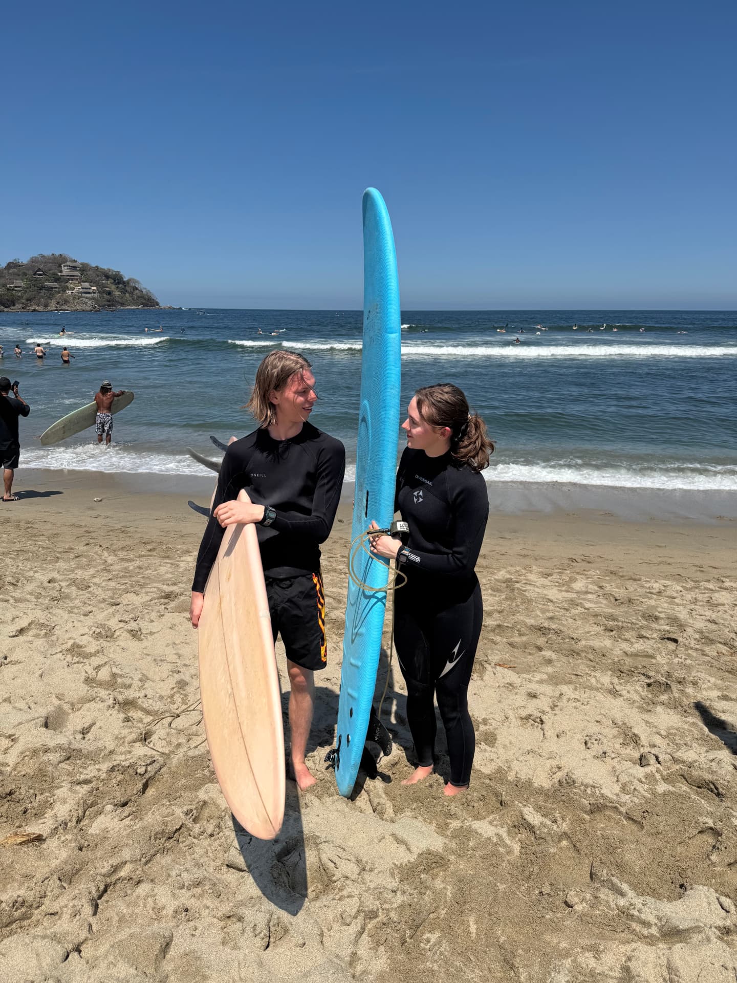 Owen and Alyson holding surfboards on a sunny beach