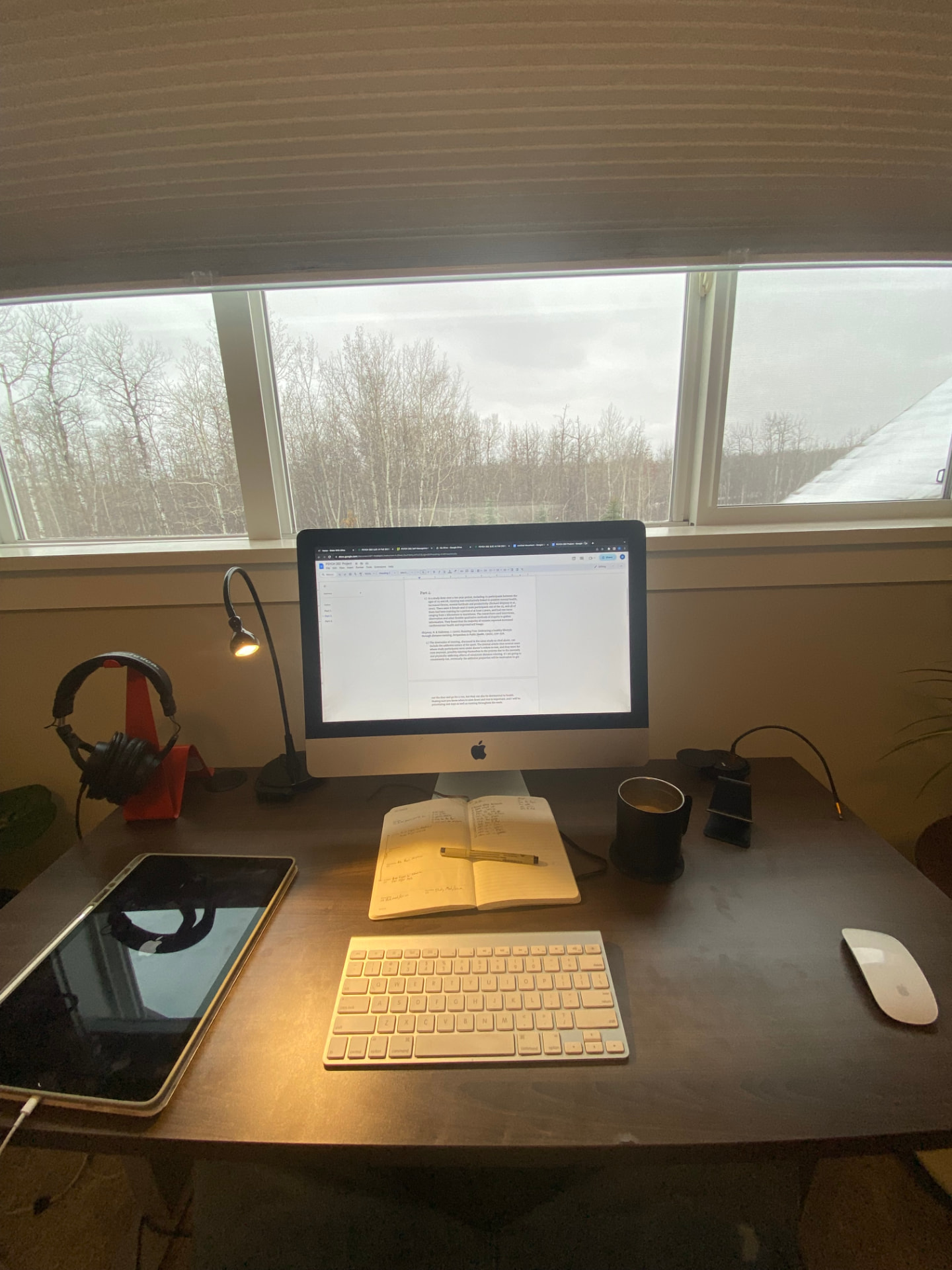 A desk with an iMac, notebook, and coffee by a window